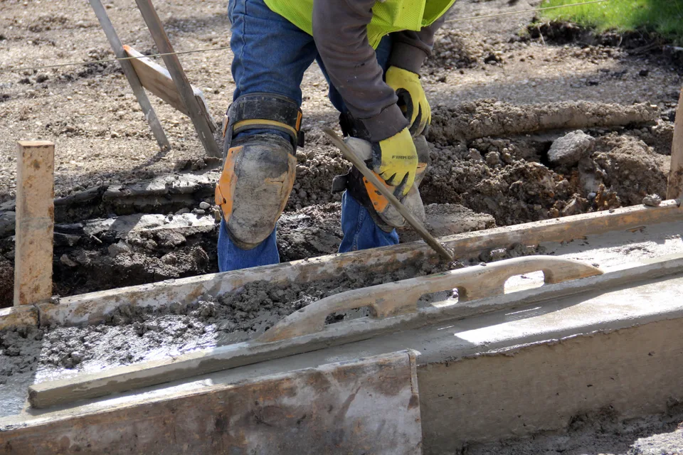 Worker leveling freshly placed concrete beside formwork